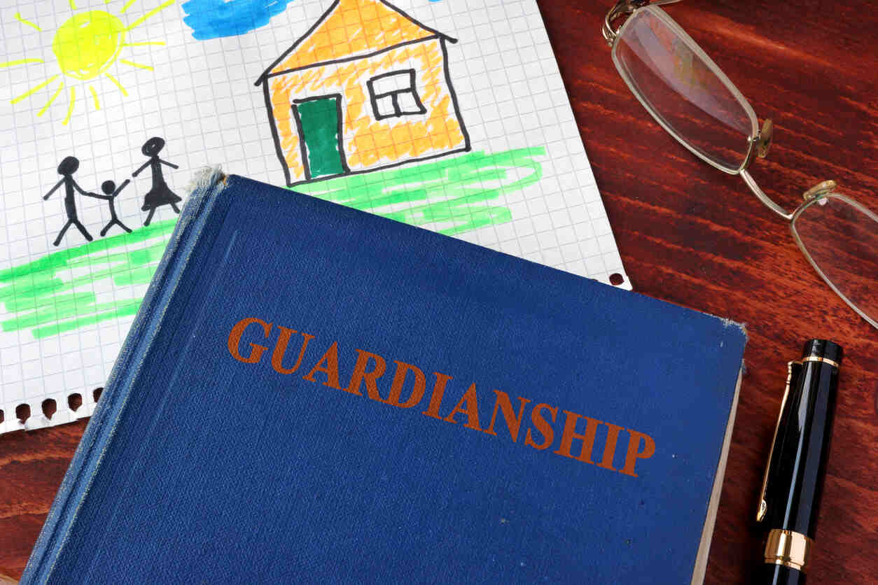 A blue book titled "GUARDIANSHIP" rests on a wooden table, next to a child's drawing of a family and house, and a pair of eyeglasses, symbolizing the legal aspects of guardianship.